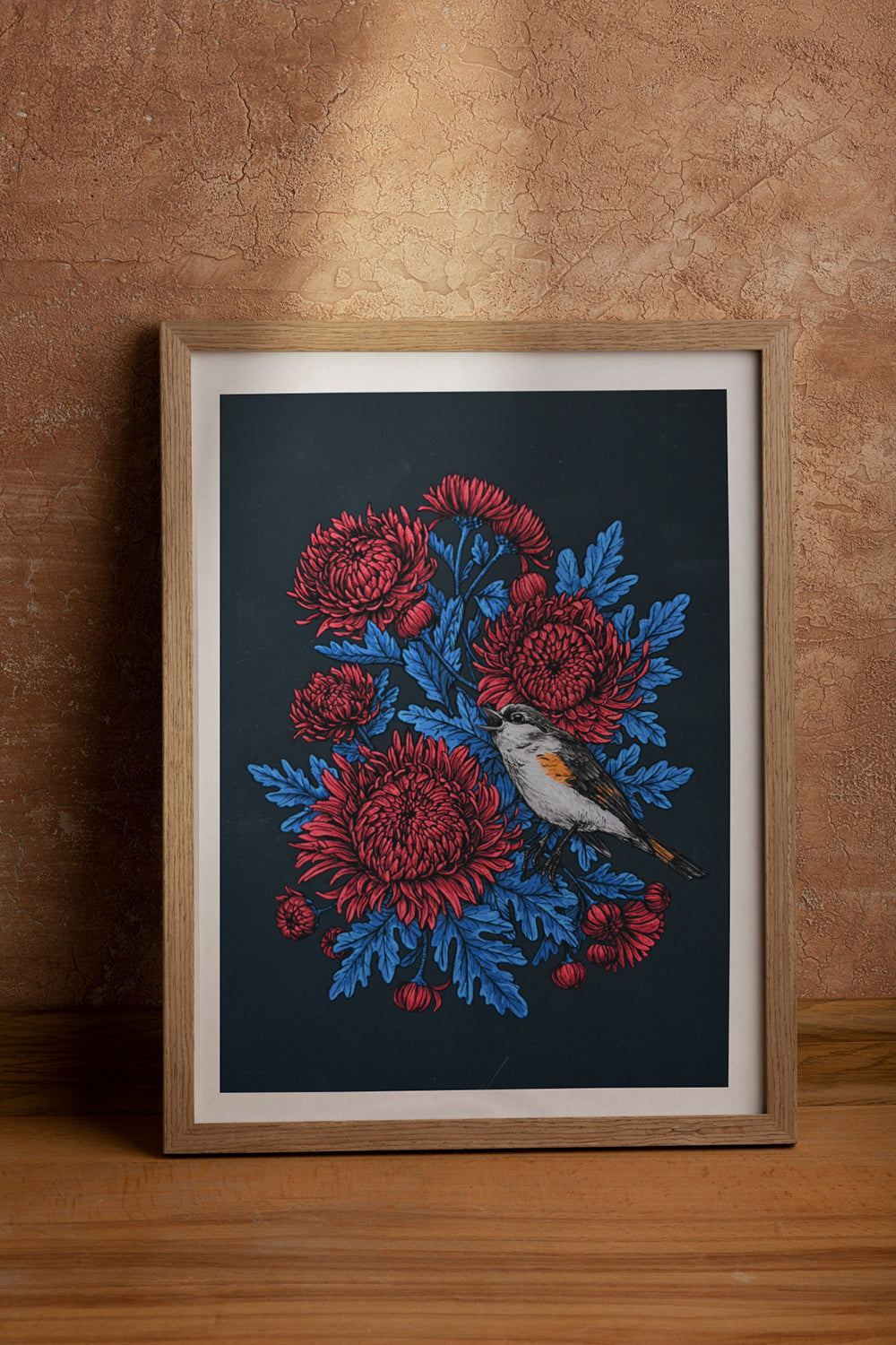 Framed print with red chrysanthemums and blue leaves and bird on a dark background, against a brown wall.