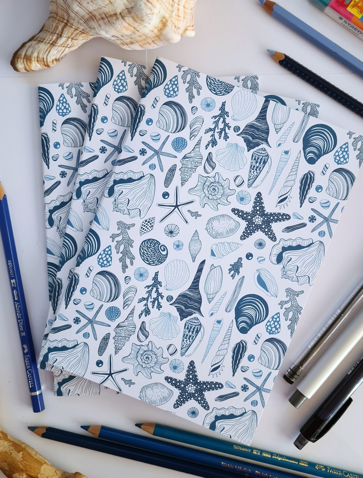 photo of 3 hand-made notebooks with hand-painted sea shells pattern print on the cover