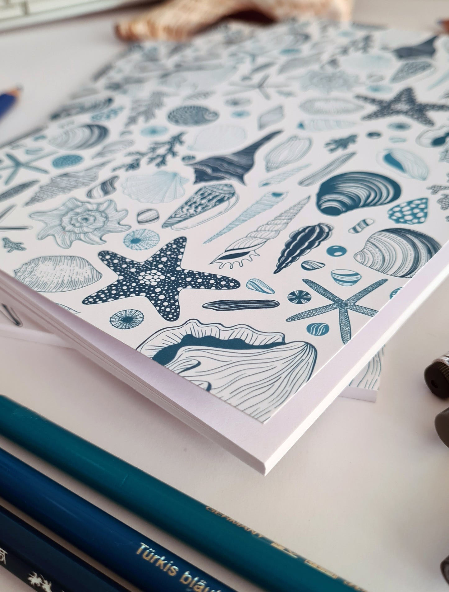 photo of hand-made notebook with hand-painted sea shells pattern print on the cover, close up on the corner