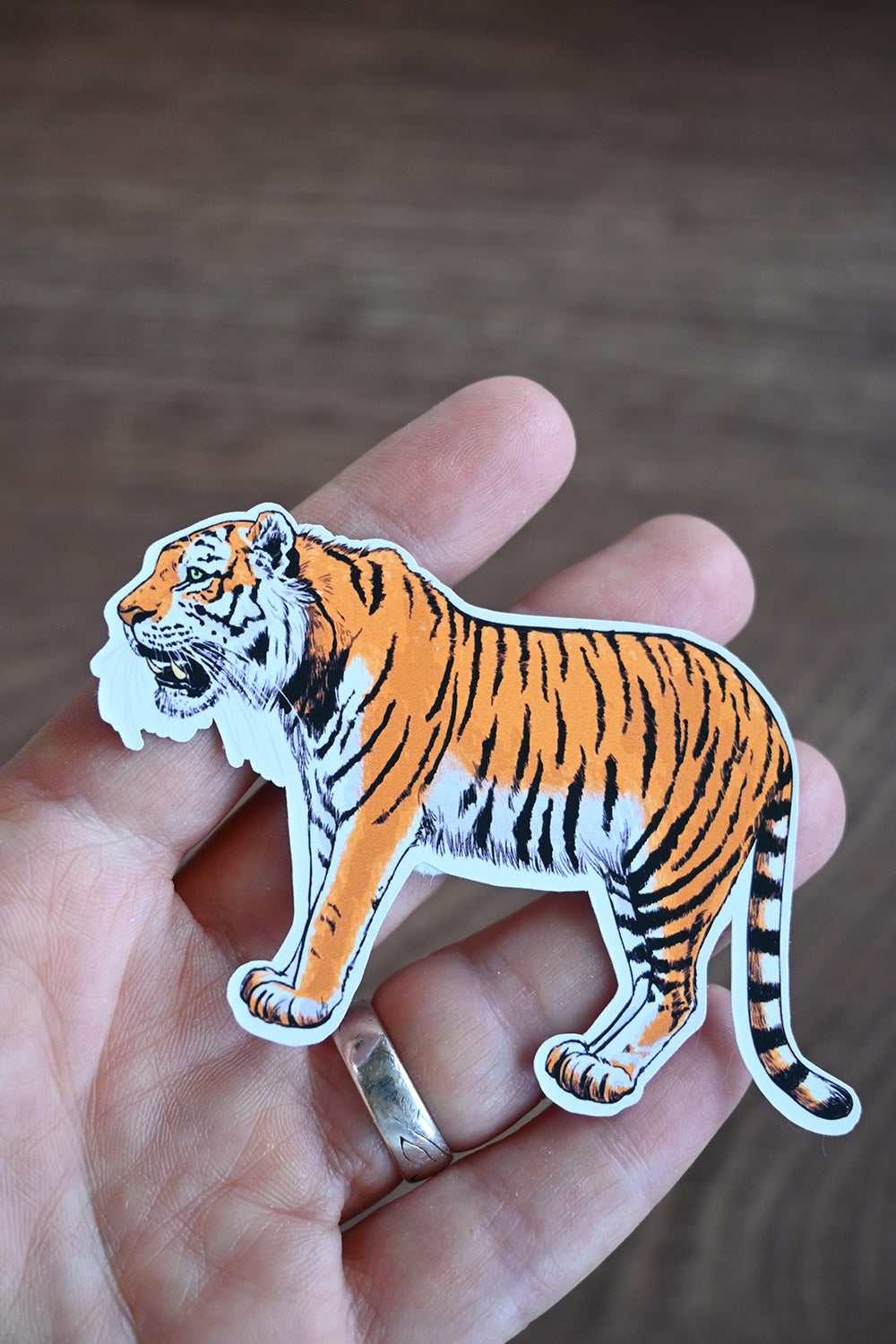 Sticker of a tiger held between fingers against a blurred background
