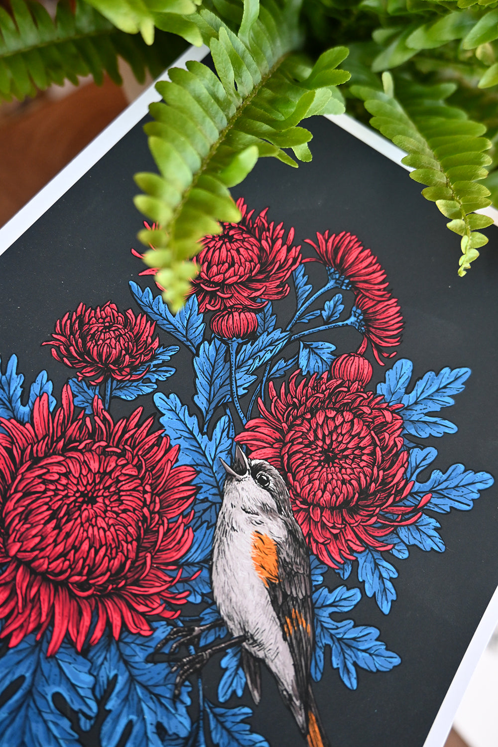 Artistic depiction of a bird among red and blue flowers on a black background, with green leaves in the foreground.