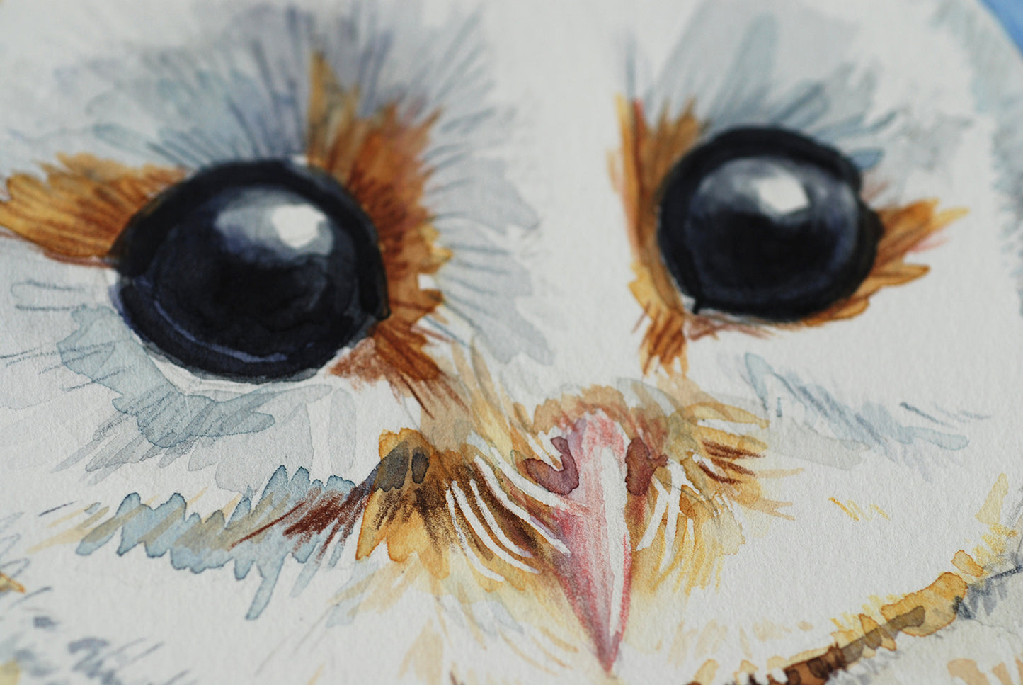 Close-up of a watercolor painting of an owl's face with large eyes and detailed feathers.