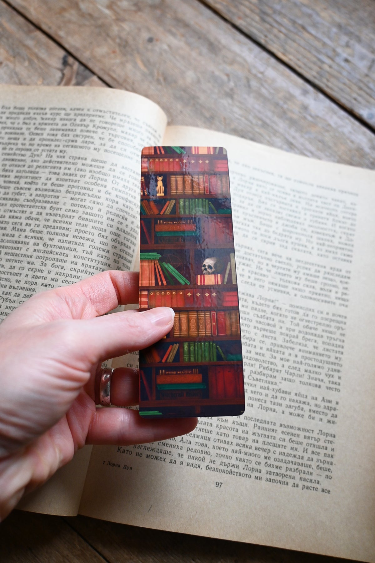 Hand holding a colorful bookmark with book design on an open book