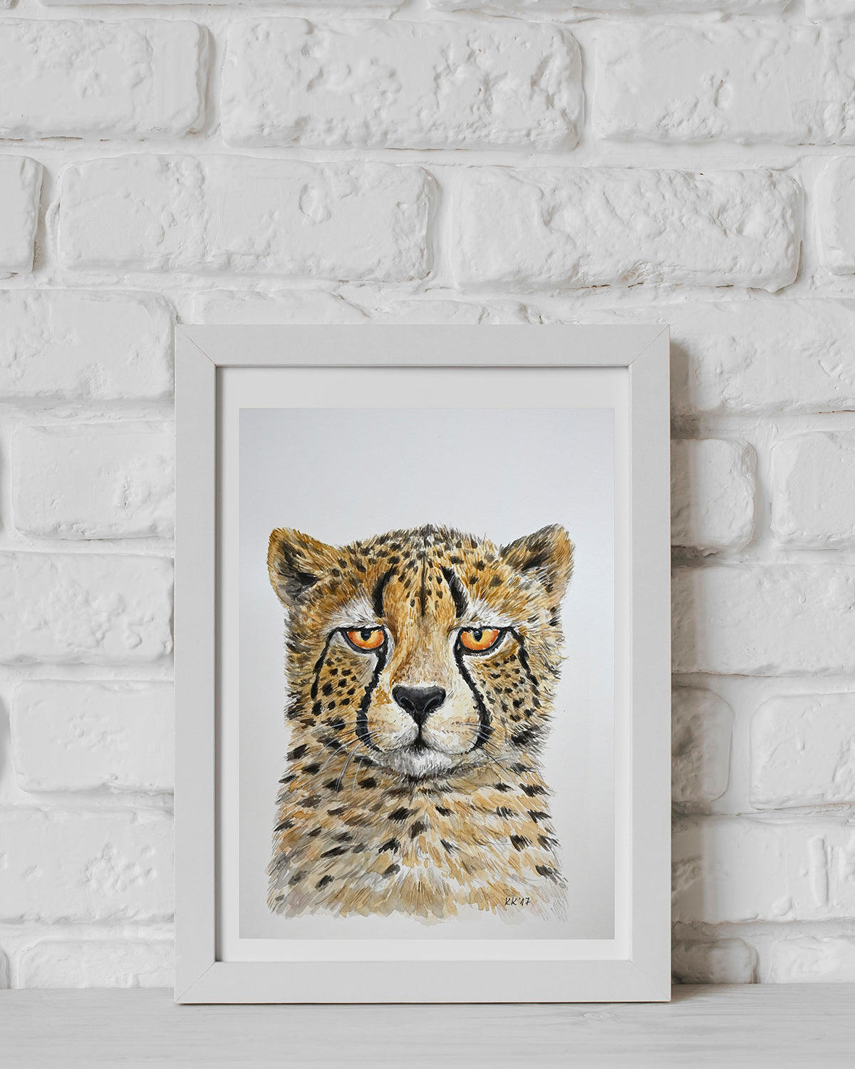 Framed artwork of a cheetah's face on a white brick wall background