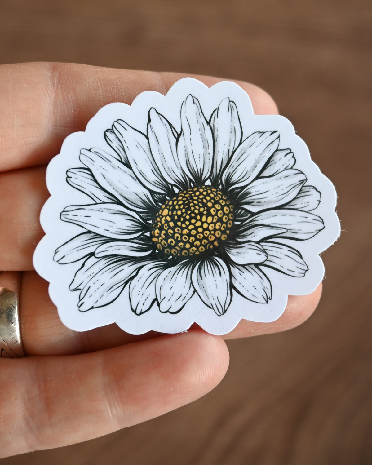Hand holding a white daisy sticker against a brown background