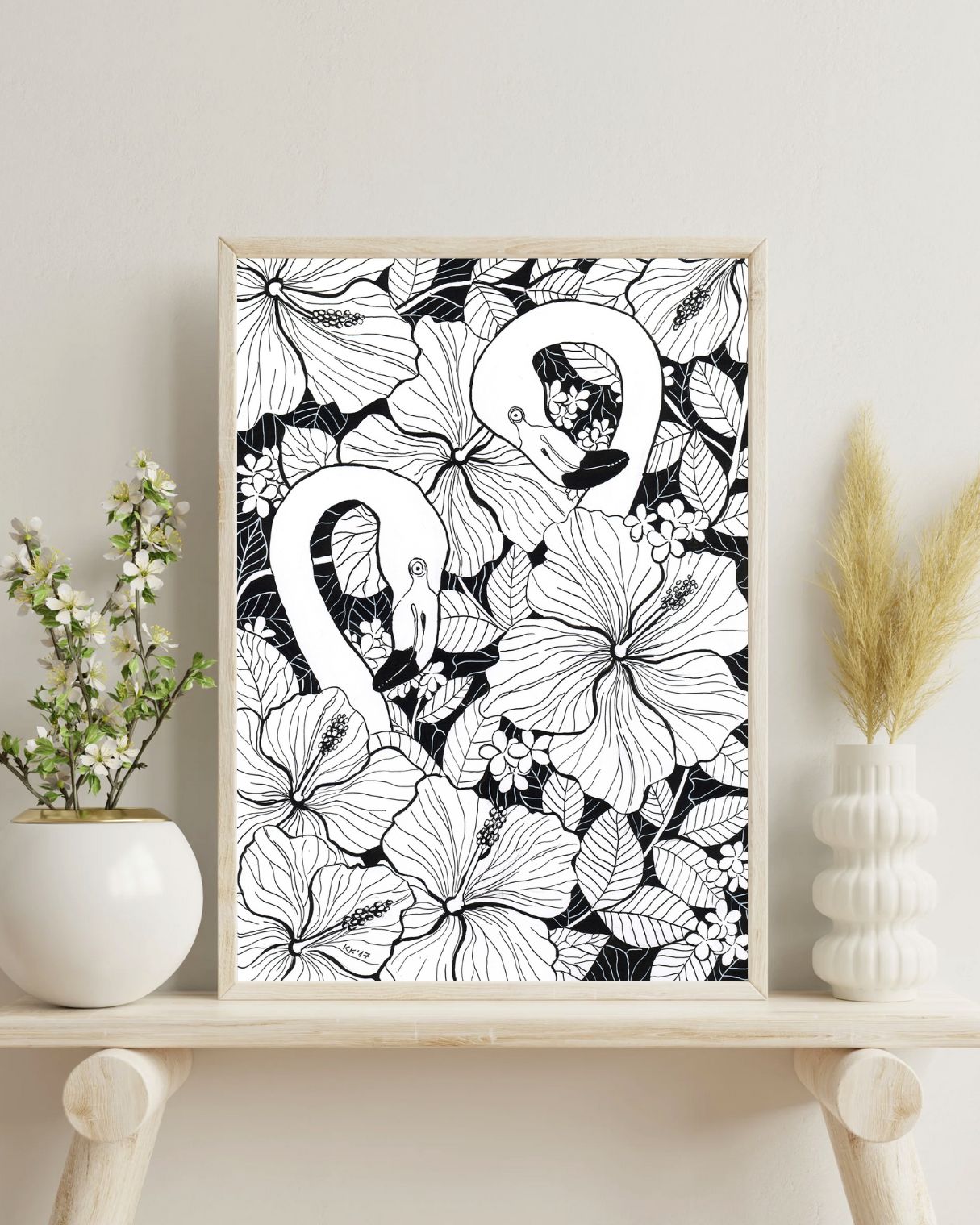 Framed black and white floral and flamingo artwork on a shelf with decorative items.