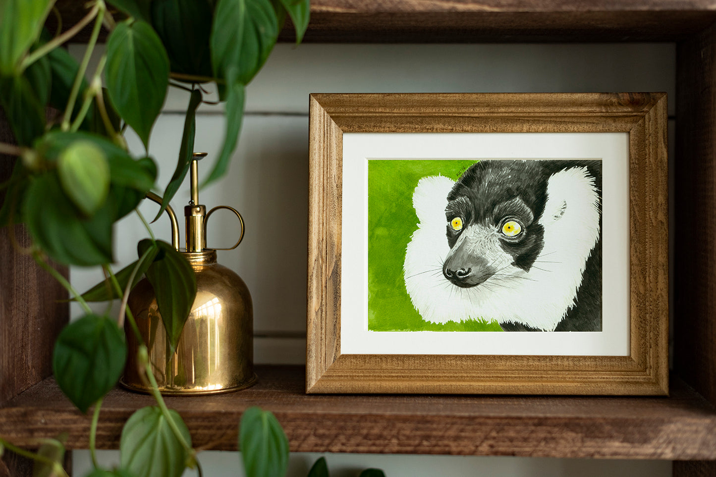 Framed artwork of a lemur on a wooden shelf with plants and a gold lamp.