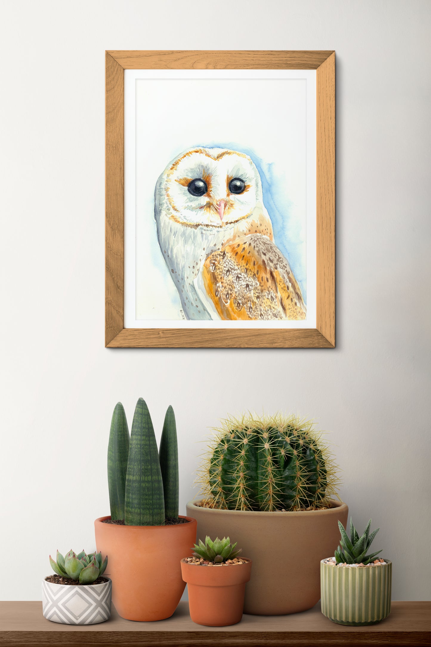 Framed artwork of an owl on a wall above a shelf with potted plants.