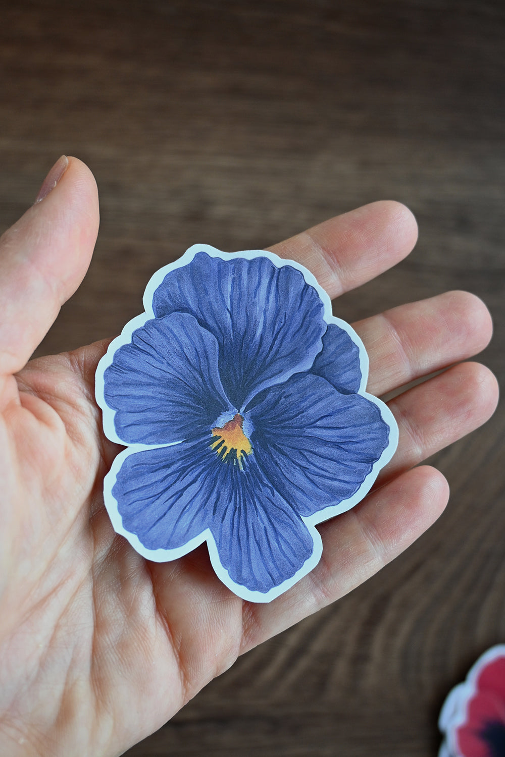 Hand holding a blue pansy sticker with a blurred background