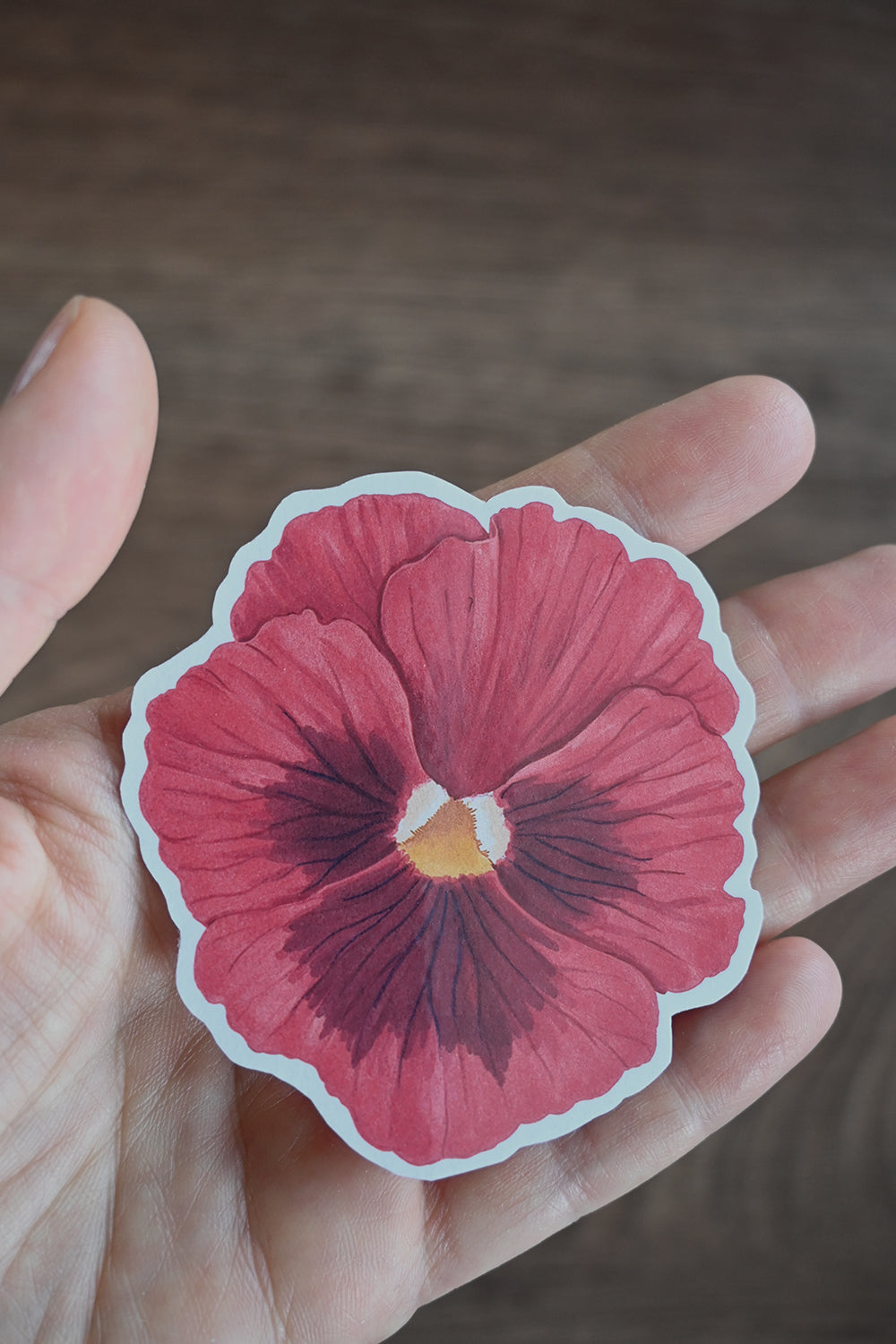 Hand holding a red pansy sticker against a blurred background