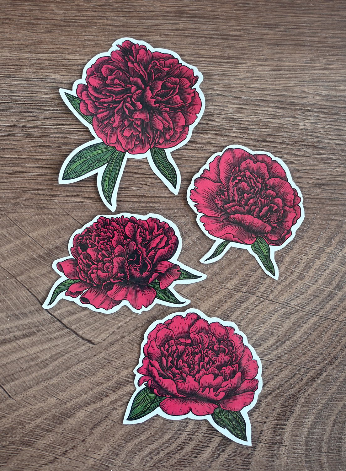 Four red peony stickers on a wooden surface