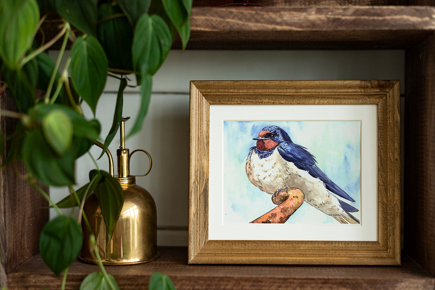 Framed artwork of a swallow on a wooden shelf with a plant and a brass container.