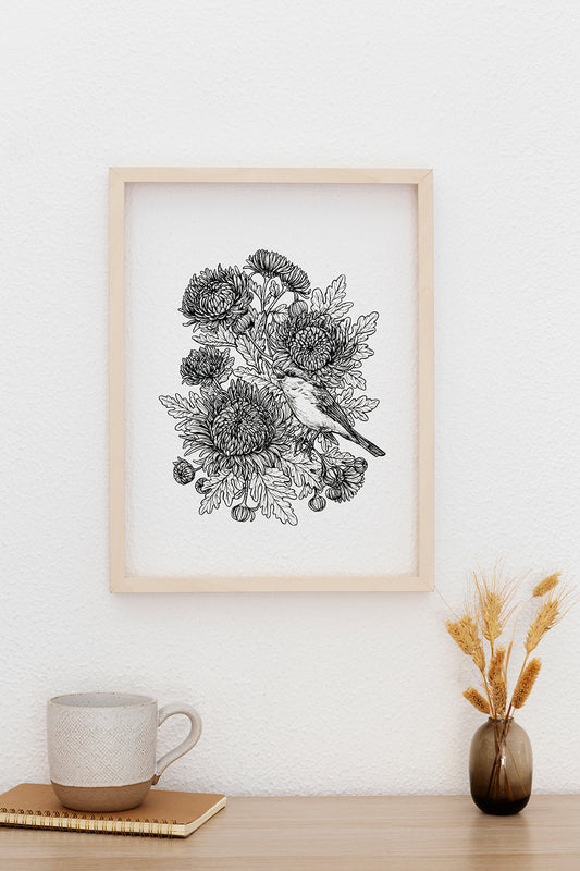 Framed black and white floral and bird illustration on a wall above a wooden table with a mug and vase.