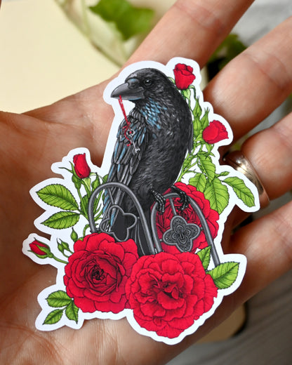 photo of a vinyl sticker with printed illustration of a raven perching on a ornate fence and holding ribbon with a key in it's beak