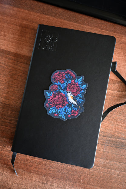 Black notebook with a vinyl sticker with red mums and a restart bird on a wooden surface