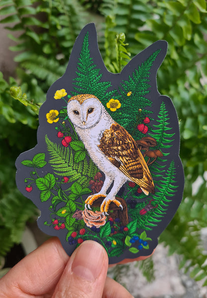 Sticker of an owl surrounded by foliage held in front of a green leafy background