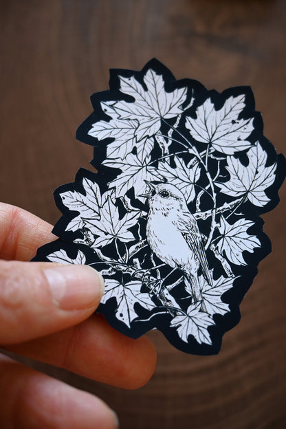 Decorative sticker with a bird and leaves held by a hand on a wooden surface