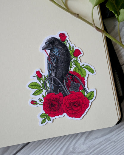 photo of a vinyl sticker with printed illustration of a raven perching on a ornate fence and holding ribbon with a key in it's beak