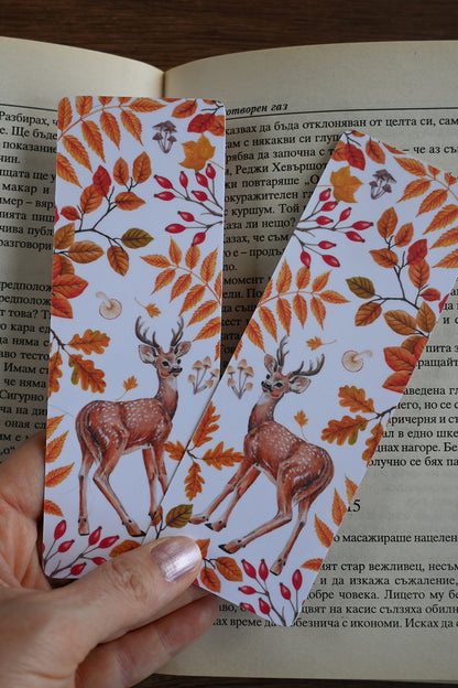 Two deer-themed bookmarks with autumn leaves held over an open book.
