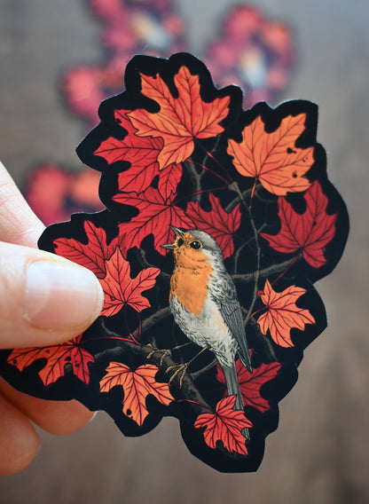 Sticker of a bird among red leaves held by a hand with a blurred background
