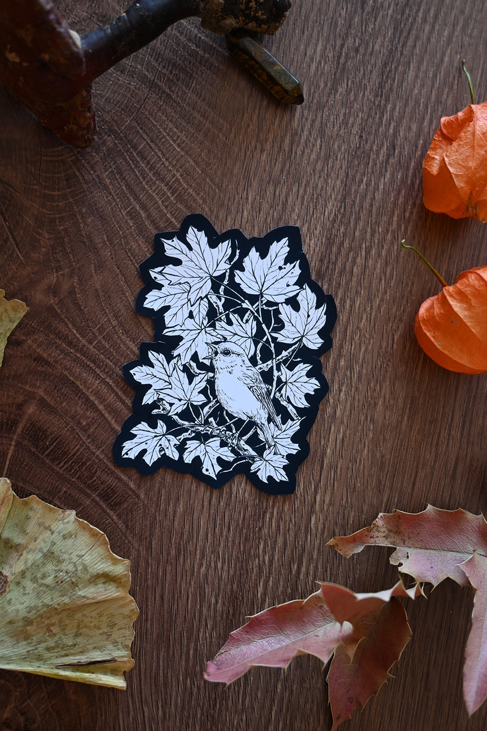 Black and white leaf and bird design patch on a wooden surface with leaves.