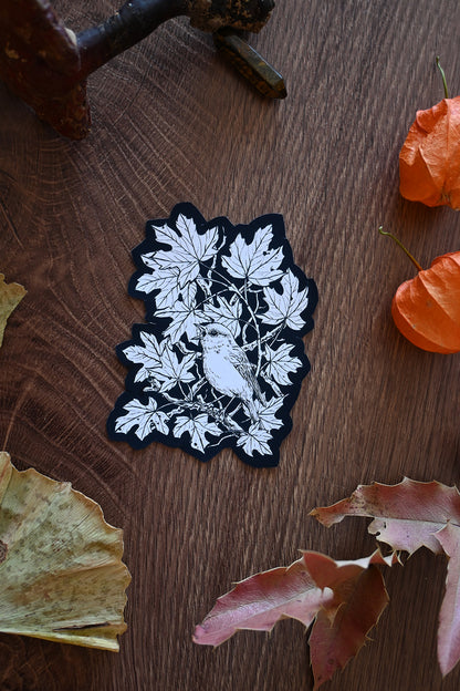 Black and white leaf and bird design patch on a wooden surface with leaves.