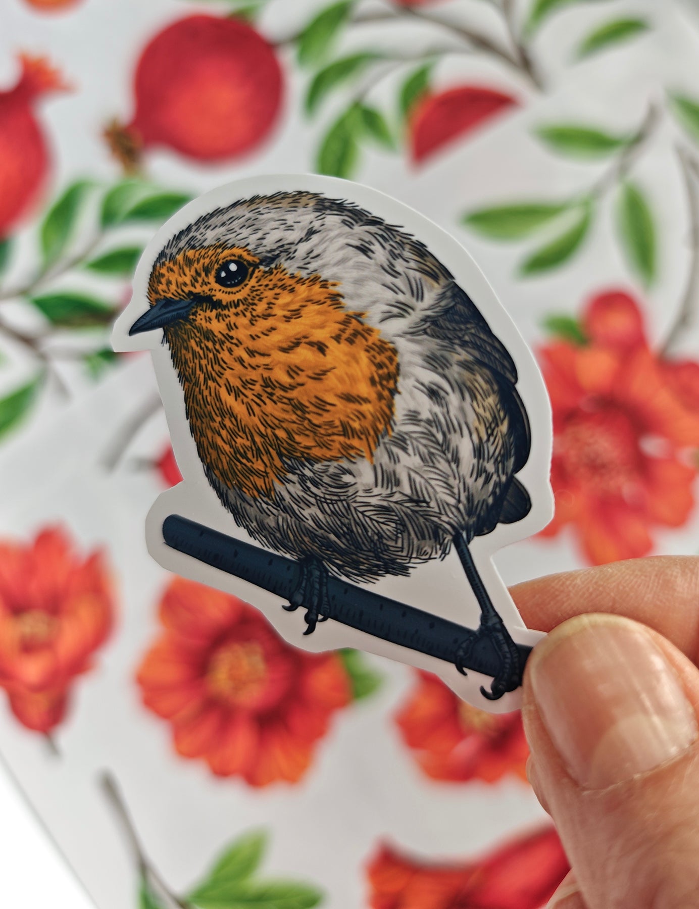 Photo of a sticker with robin bird illustration on a patterned background with red fruit and blooms