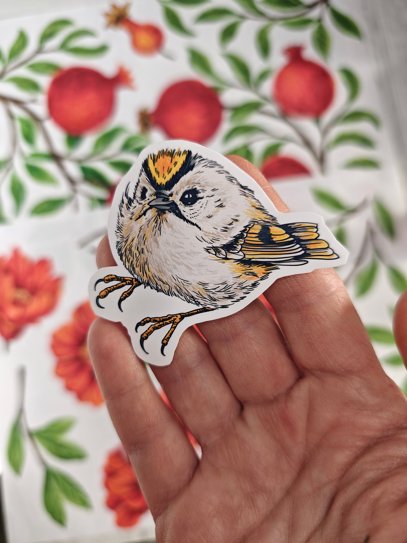 Photo of a sticker with goldcrest bird illustration on a patterned background with red fruit and blooms