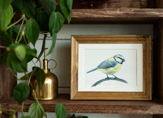 Framed artwork of a bird on a wooden shelf with plants