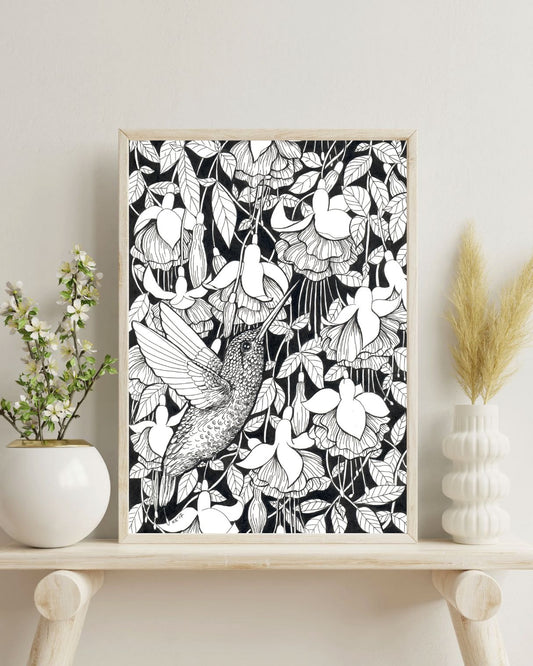 Framed black and white ink drawing of a hummingbird and fuchsia on a shelf with decorative items.