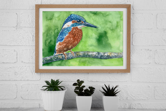 Framed artwork of a kingfisher bird on a branch with green background, displayed on a white brick wall.