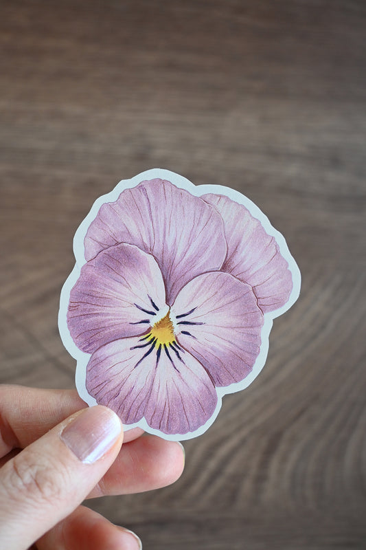Hand holding a pansy flower sticker on a wooden surface
