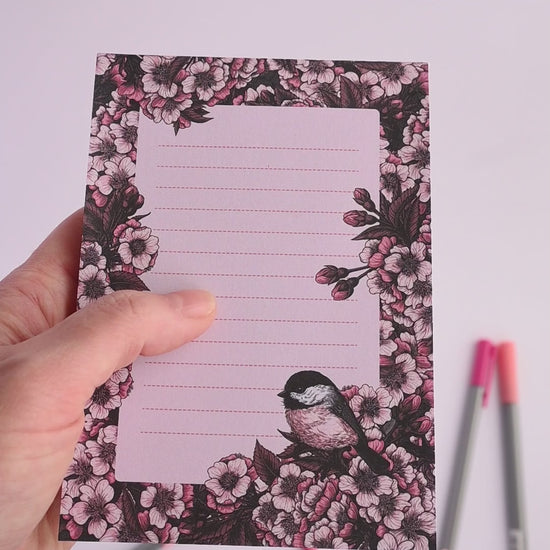 video of notepad featuring hand painted frame of cherry blosssom and chicakee bird in the lower right corner and  lined middle